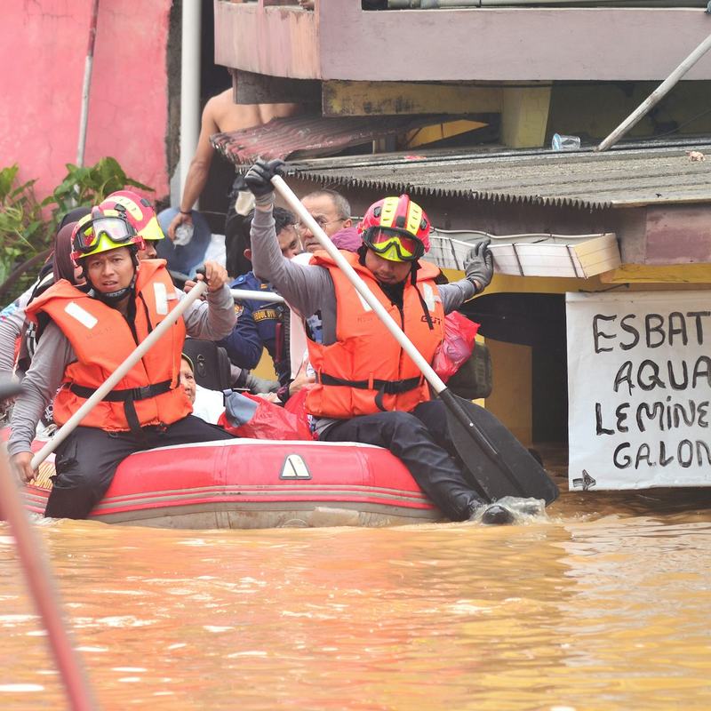 Equipe de resgate navegando de bote por uma rua alagada.
